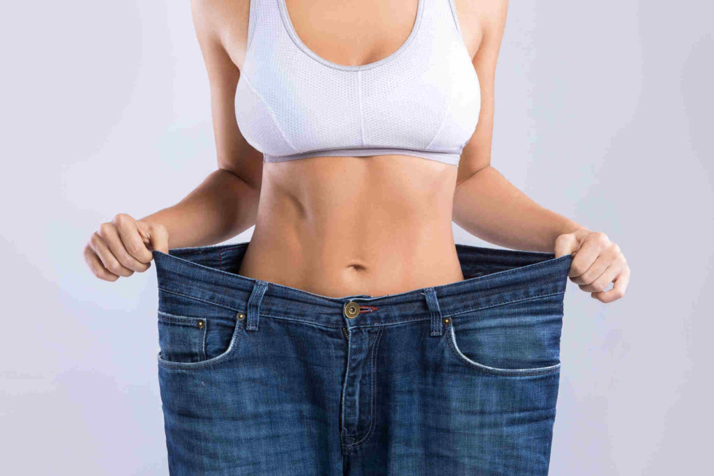 Alpilean_happy-woman-wearing-jeans-after-weight-loss-on-gray-background